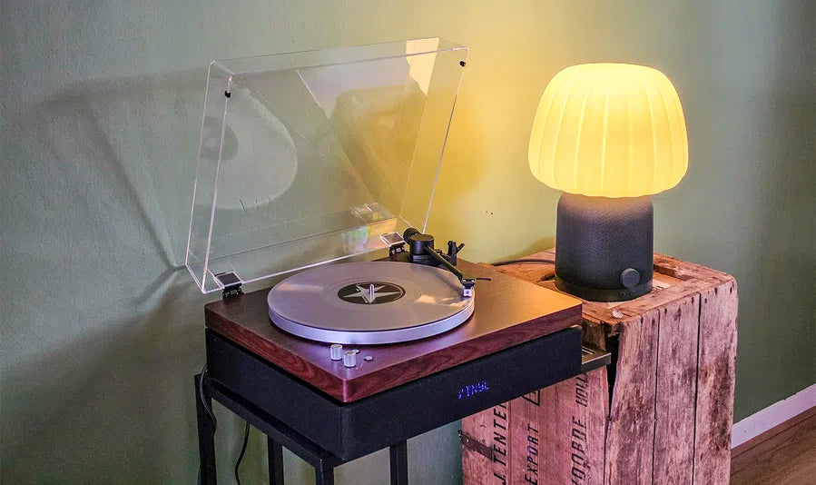 Aulo platenspeler met geopende stofkap naast een warme tafellamp in een rustig interieur, sfeerbeeld bij de review van Bright