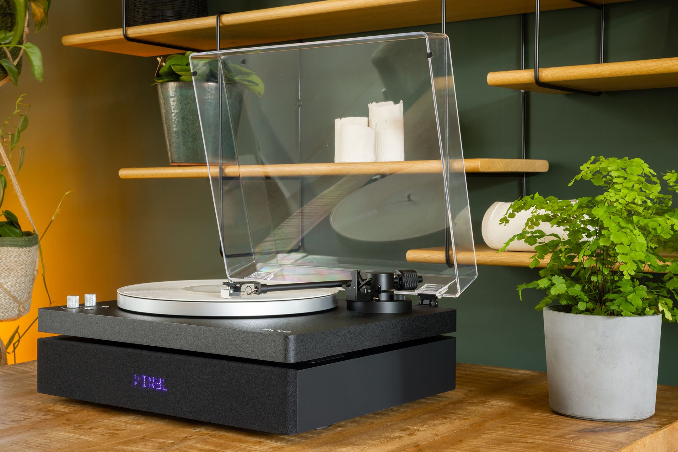 Zwarte Aulo platenspeler met geopende stofkap in een warm interieur met planten en een houten wandrek