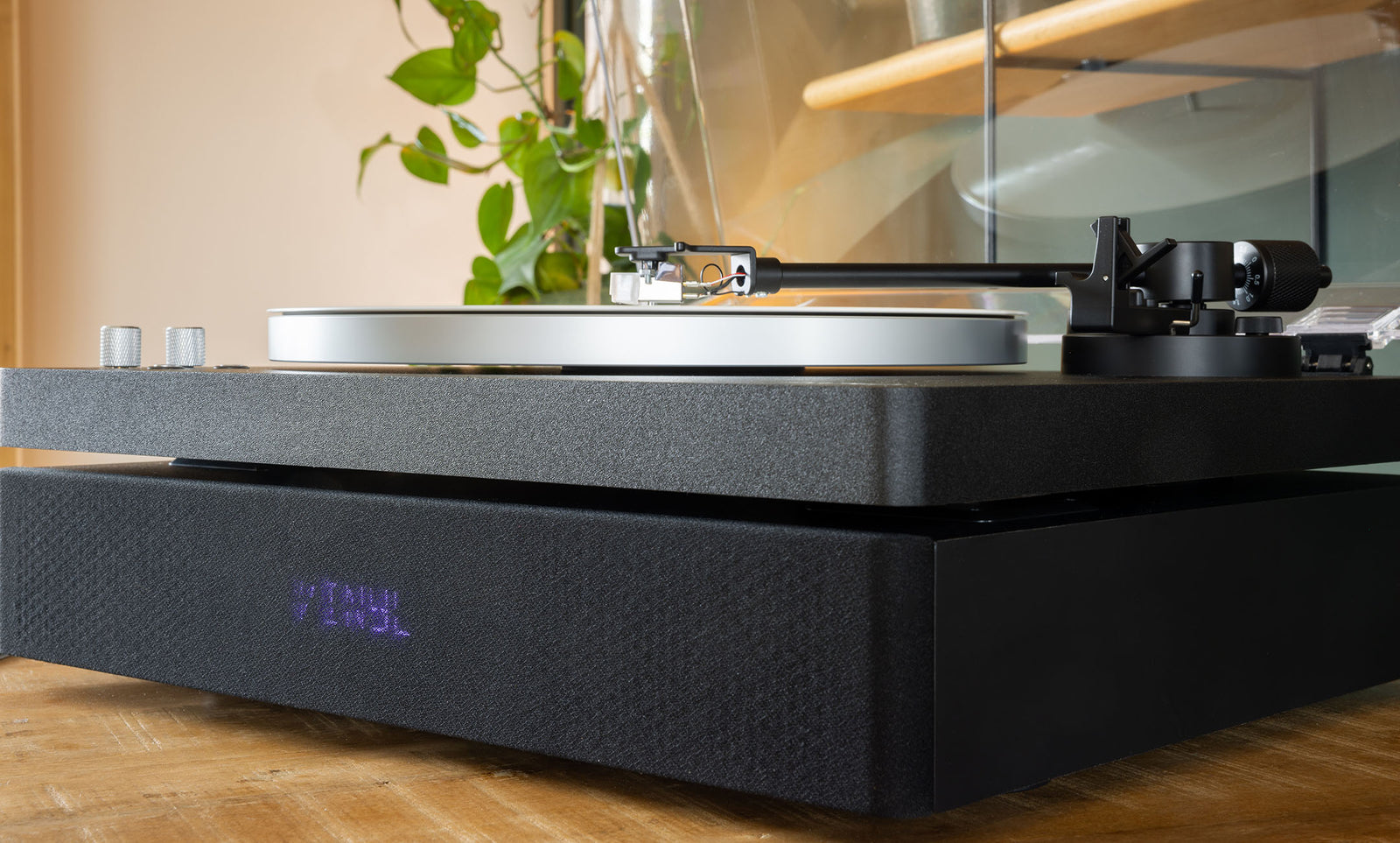 Zijaanzicht van de zwarte Aulo, waar de draaitafel losgekoppeld boven de speakerbasis zweeft, met oplichtend VINYL-display