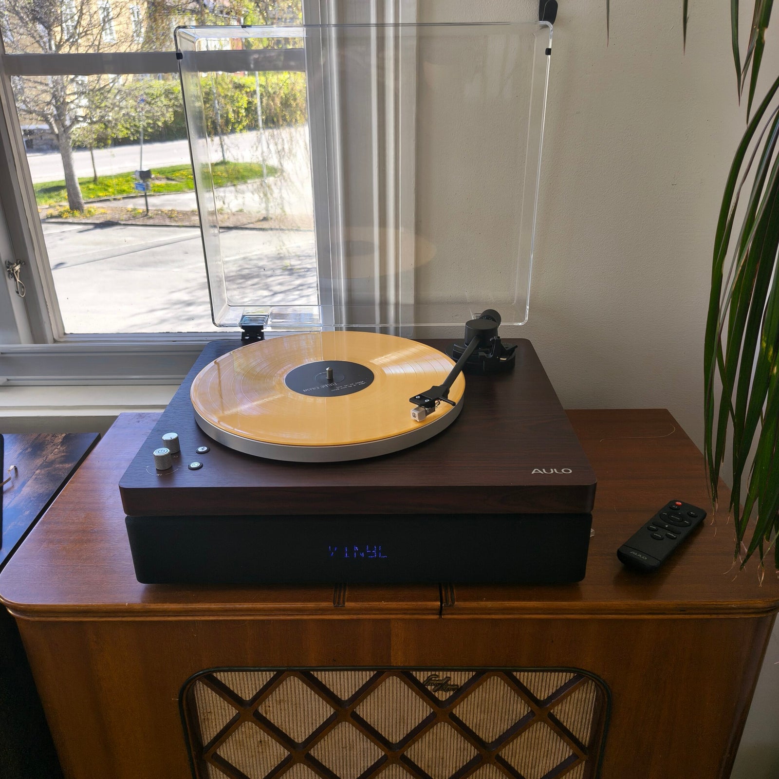Close-up van de Aulo platenspeler met toonarm, naast een antieke houten radiomeubel