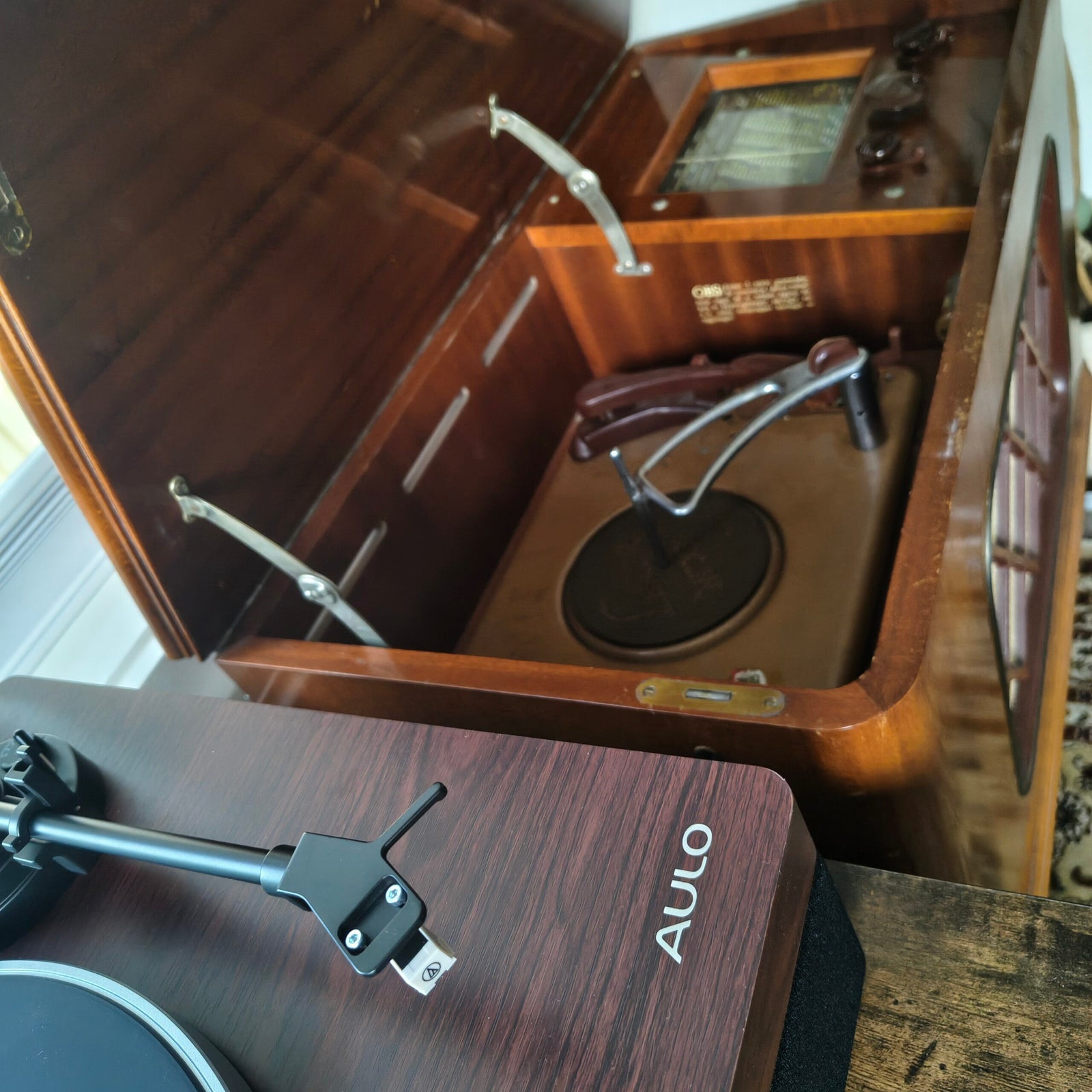 Close-up van de toonarm en het element van de Aulo, met een geopend vintage radiomeubel op de achtergrond