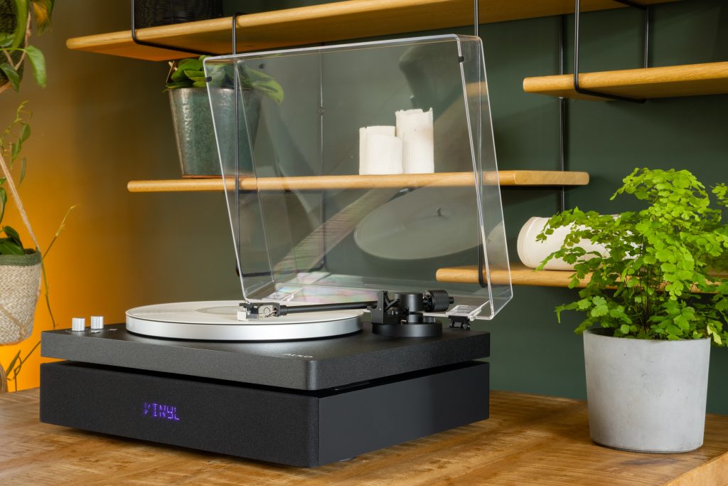 Zwarte Aulo all-in-one platenspeler met opgeklapte stofkap tussen planten en open rekken